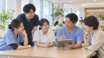 世代の異なる医療スタッフがタブレットを囲んで話し合うイメージ